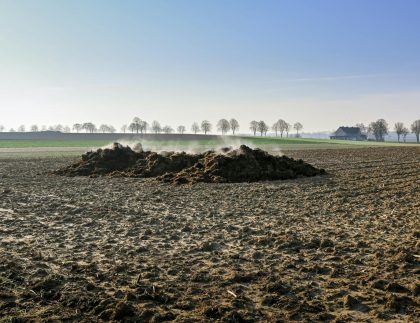 La vapeur s'élève d'un tas de fumier sur un champ labouré sous un ciel bleu clair.