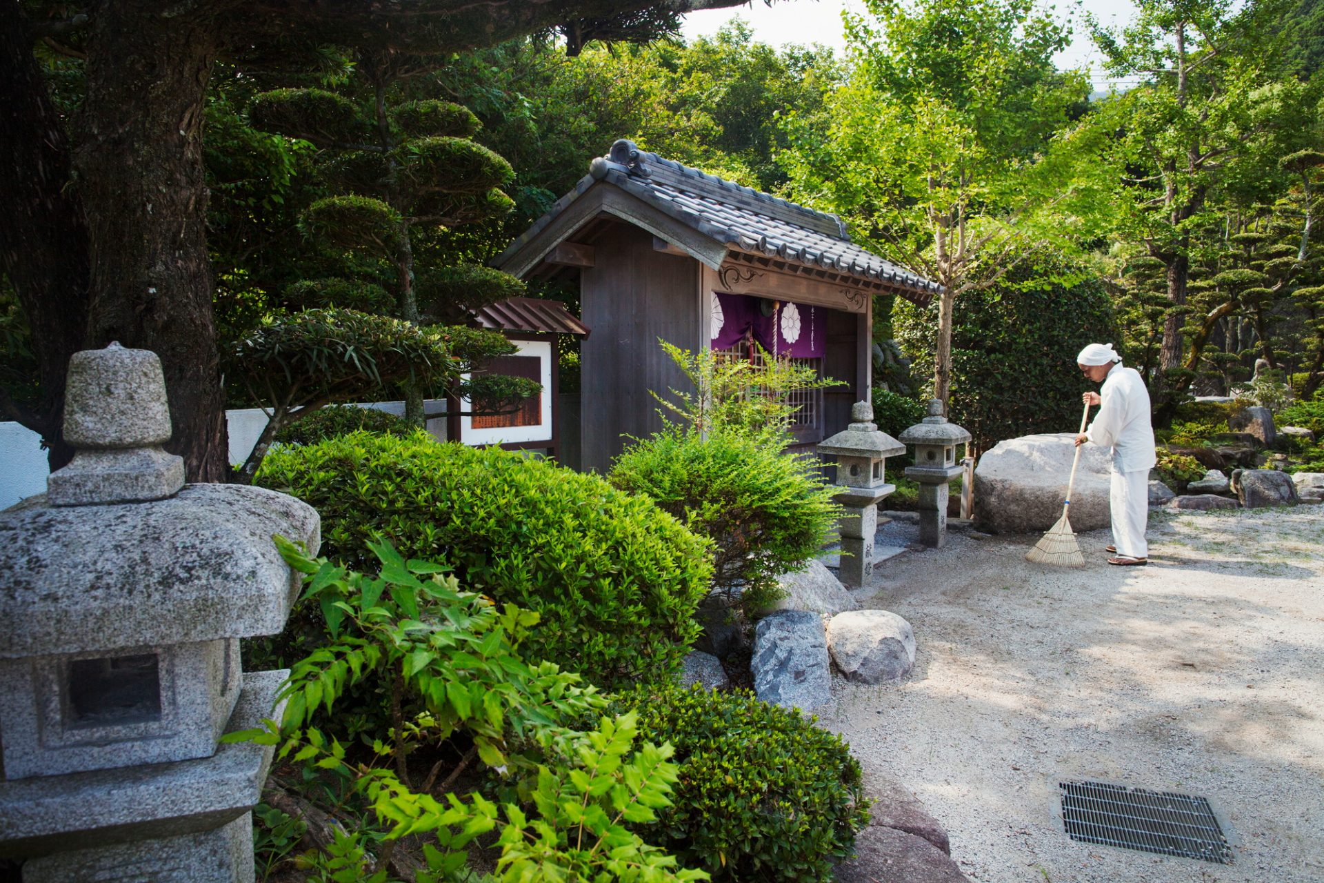 Moine bouddhiste par sanctuaire dans un jardin du temple, tenant le balai