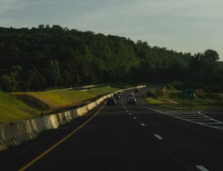 Route d'asphalte grise entre les arbres verts sous le ciel gris pendant la journée