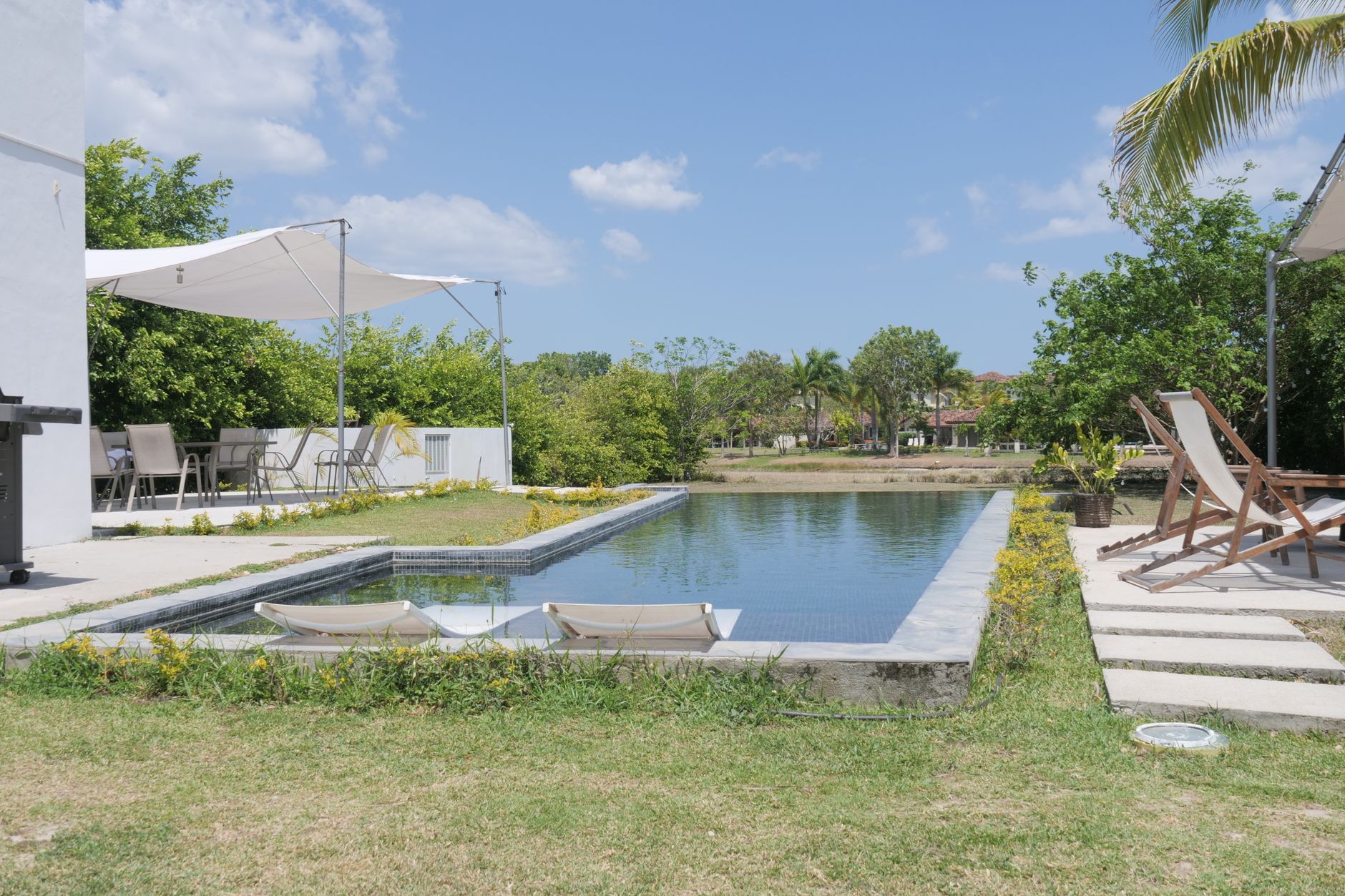 Une piscine sereine dans un hôtel de luxe, avec des chaises longues et une végétation luxuriante par une journée ensoleillée.